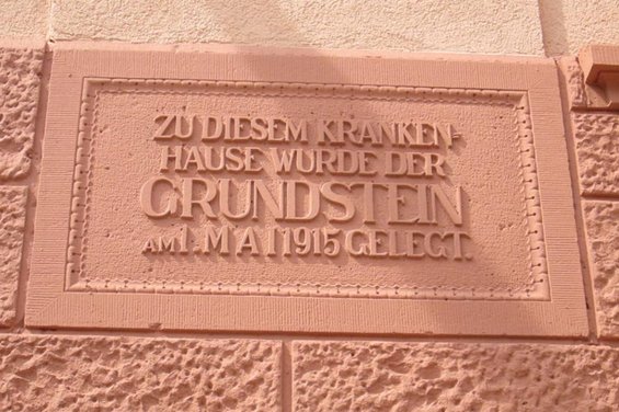Abbildung einer Wand mit der Inschrift: Zu diesem Krankenhause wurde der Grundstein am 1. Mai 1915 gelegt.