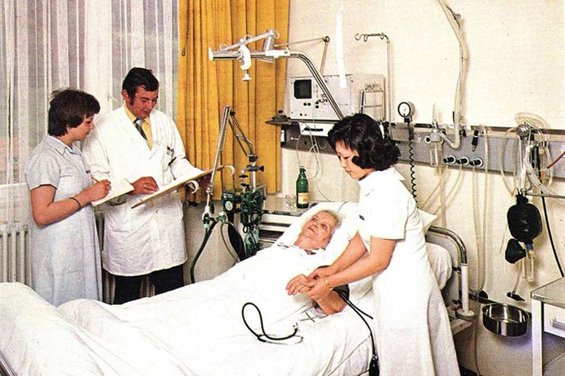 Abbildung von 3 Personen des Pflegepersonals und einer Patientin in einem Krankenzimmer