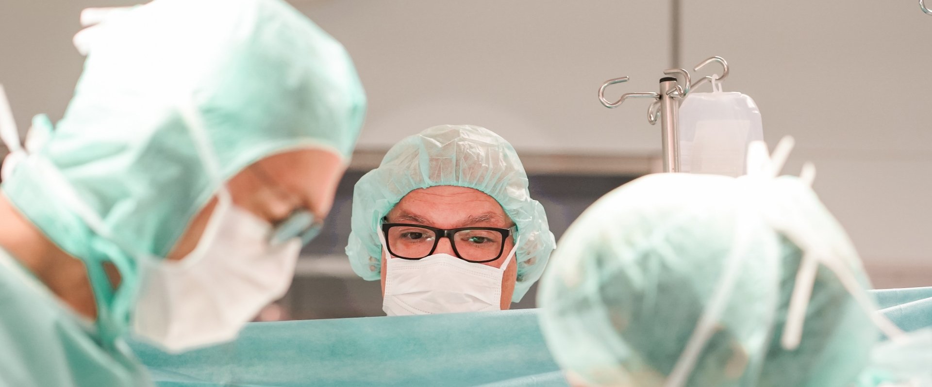 Drei Ärzte mit Maske und Haarnetz im Operationssaal