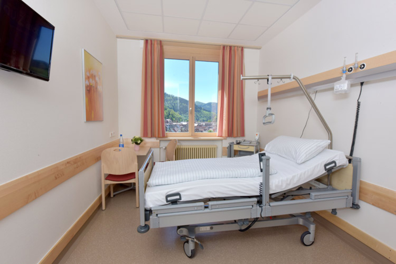 Abbildung eines Patientenzimmers mit Fernseher, Tisch und Bett